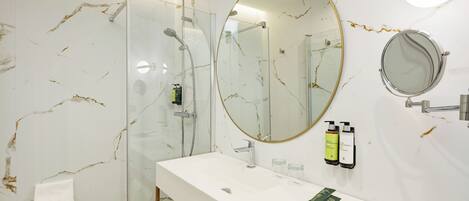 Een moderne badkamer met een douchecabine van glas, een grote spiegel en een witte wastafel met toiletartikelen.