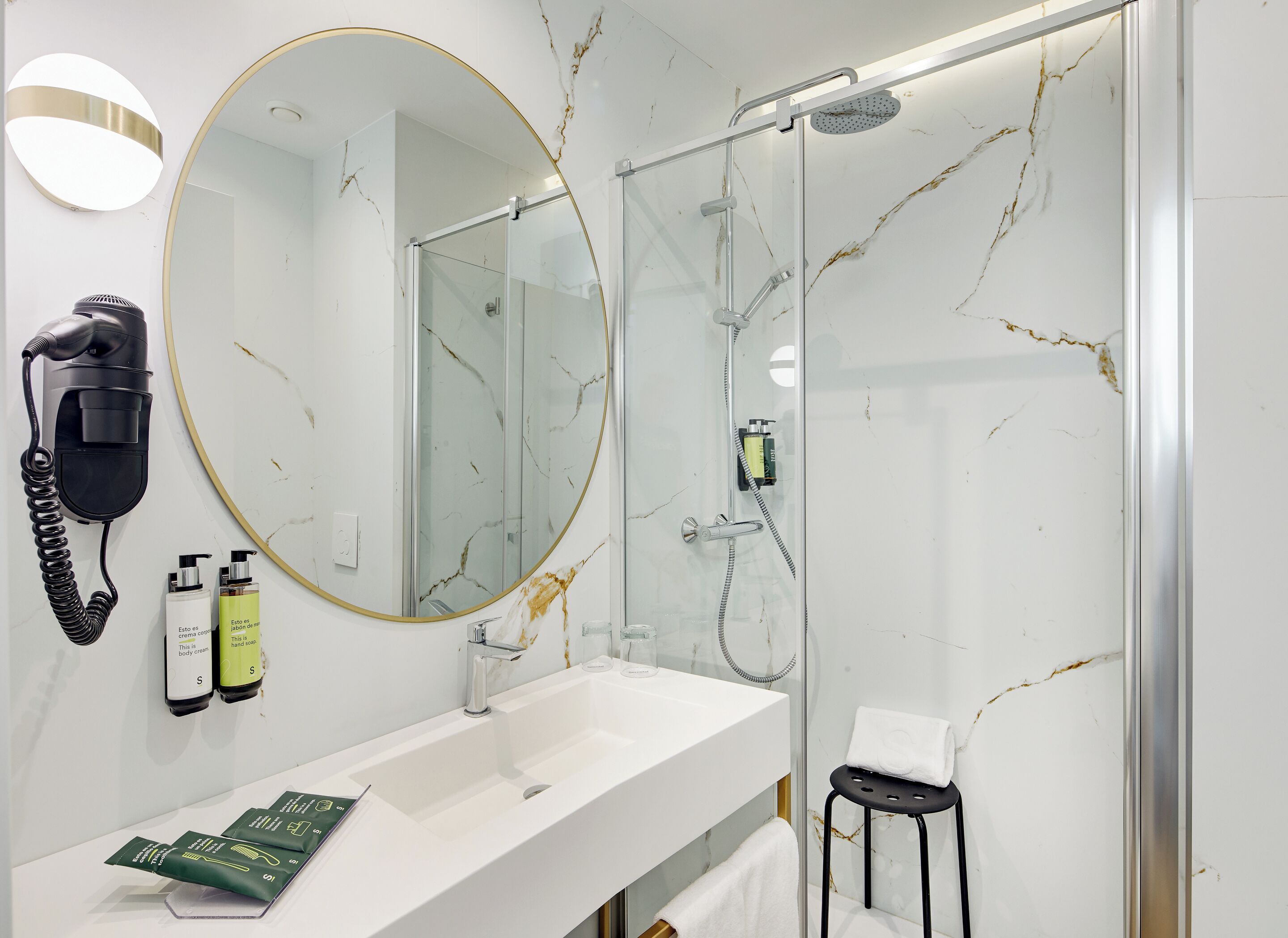 A modern bathroom with a large mirror, a hairdryer, and toiletries on the counter.