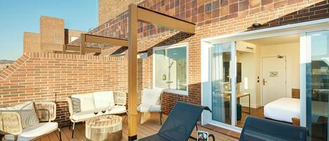 A rooftop terrace with outdoor seating, a glass-enclosed room, and a brick wall.