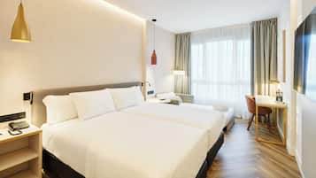 Una habitación de hotel con una cama grande, mesitas de noche, un escritorio, una silla y una ventana con cortinas.