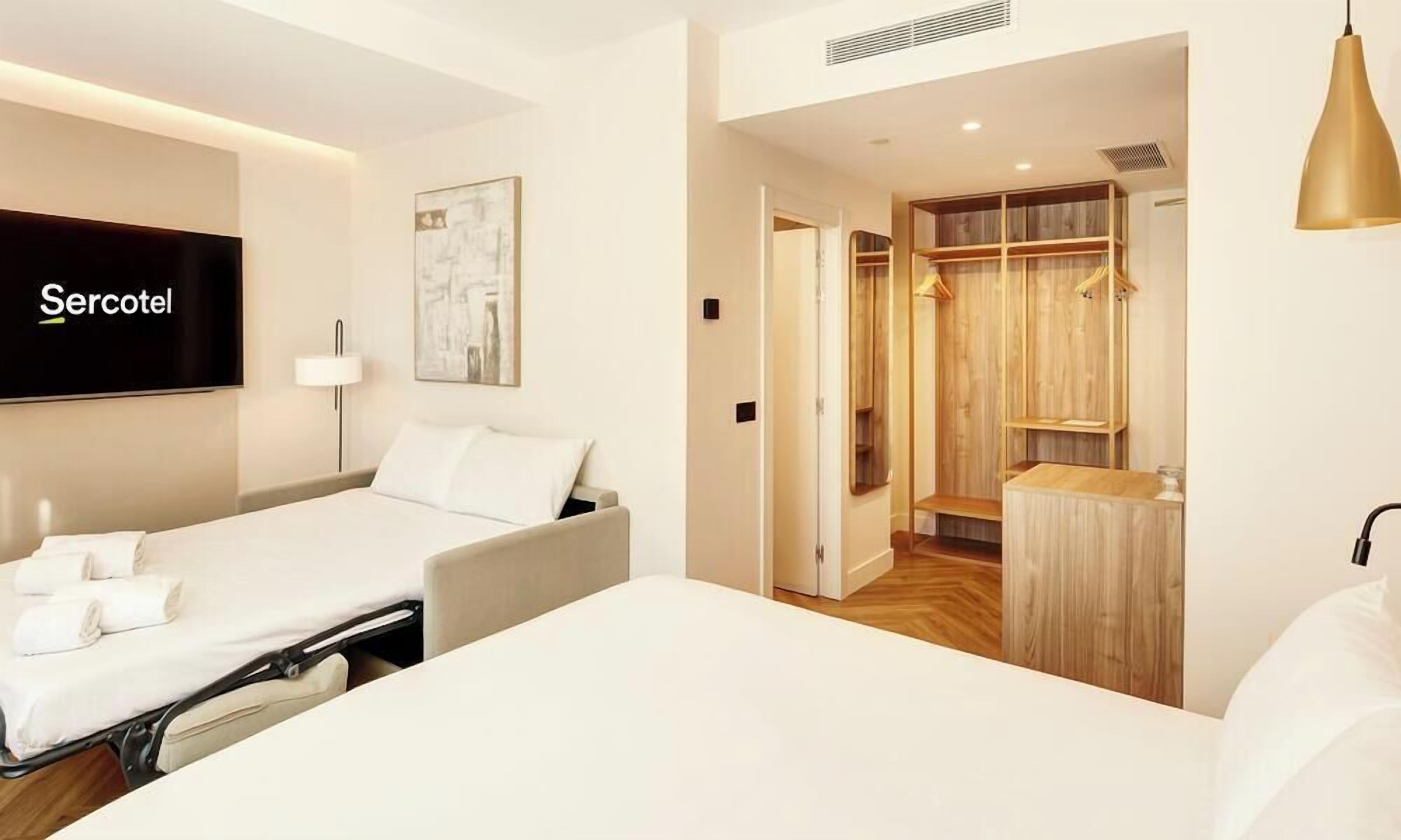 Una habitación de hotel con cama, televisor, mesita de noche, lámpara y armario.