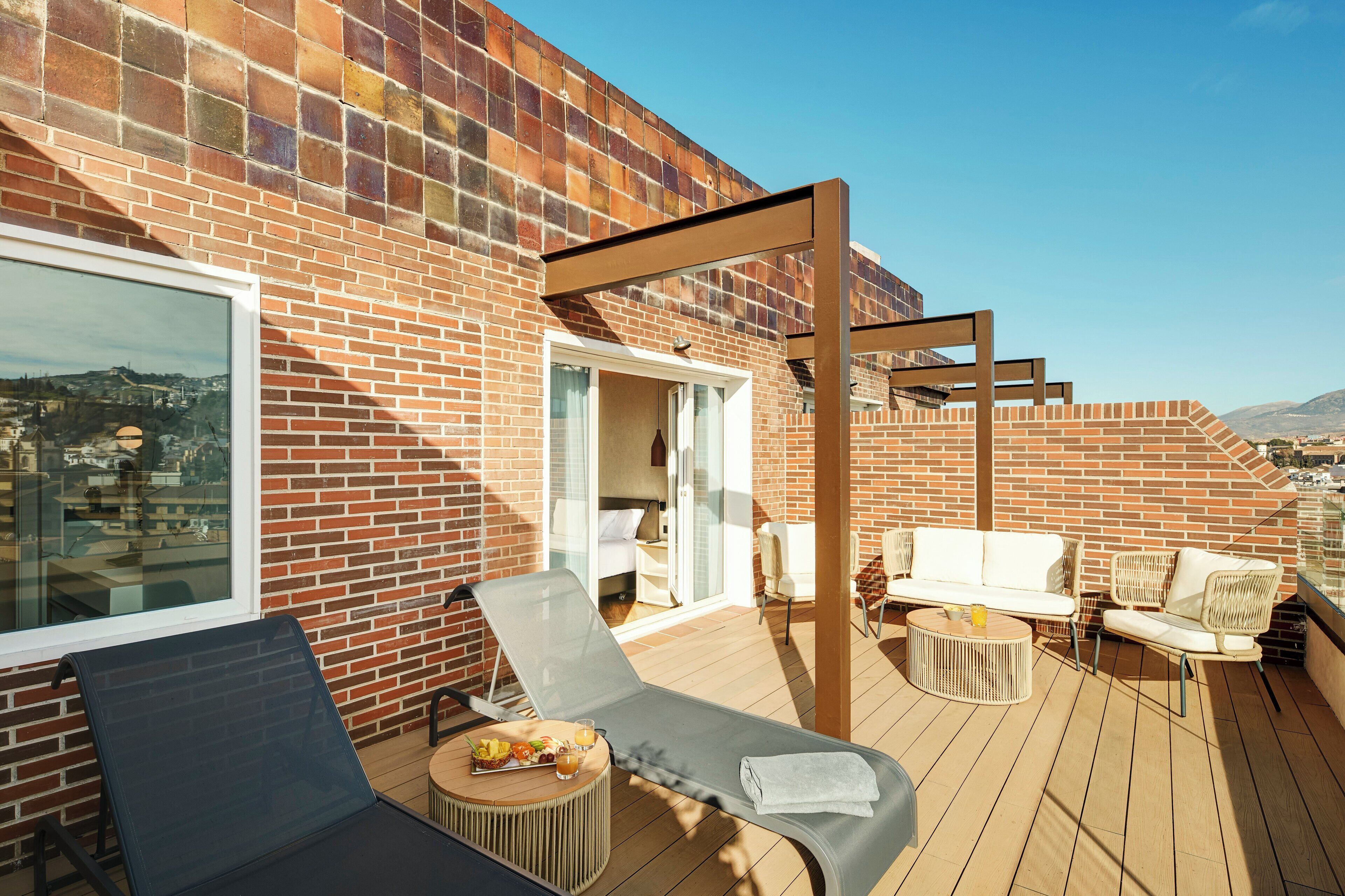 A rooftop terrace with a brick wall, a glass door leading to a room, and outdoor seating with a table and chairs.