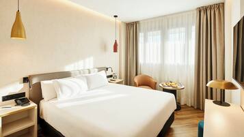 Una habitación de hotel con una cama grande, mesitas de noche, un escritorio, una silla, una pequeña mesa con desayuno y una lámpara.