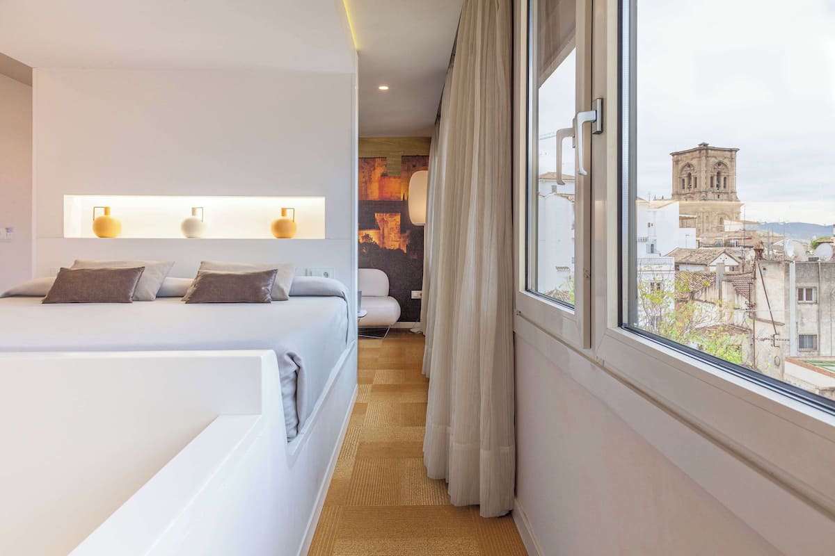 Ett hotellrum med en stor säng, utsikt över staden och en väggmonterad lampa.