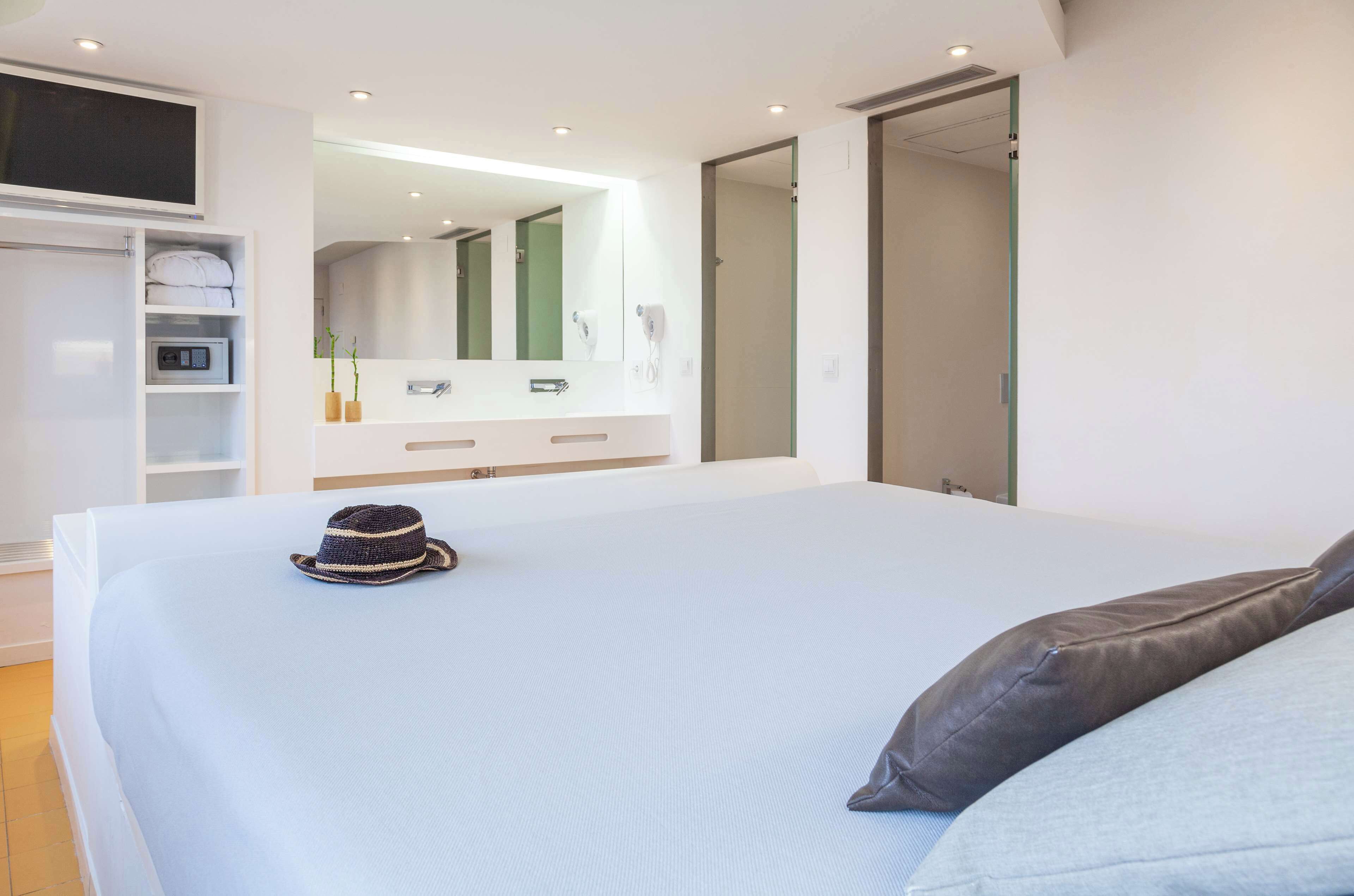 Une chambre à coucher moderne avec un grand lit, une armoire, une coiffeuse avec un miroir et un téléviseur fixé au mur.