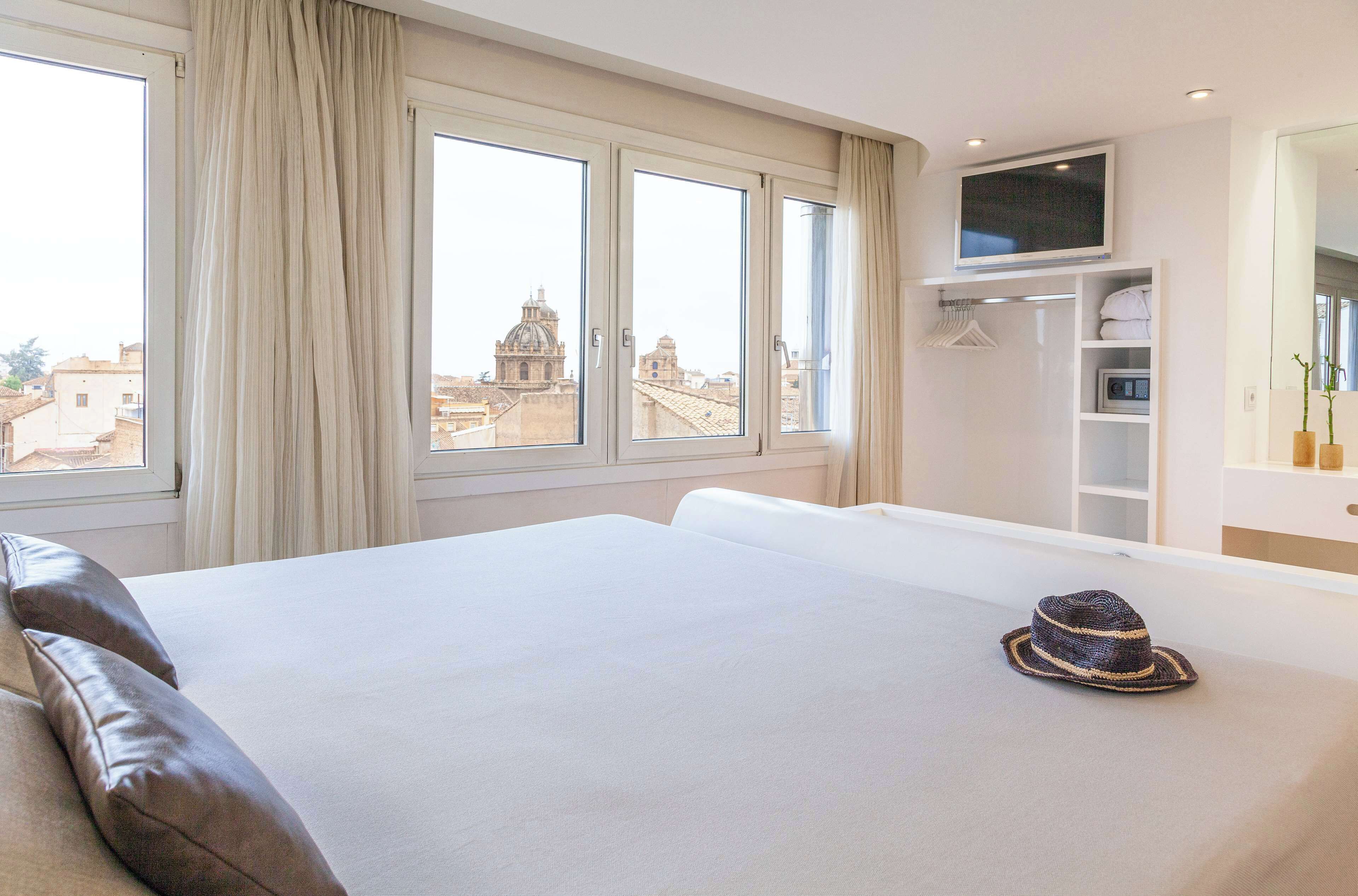 Habitación de hotel con una cama grande, televisión, armario y vistas a edificios de la ciudad.