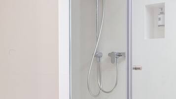 Un baño moderno con ducha envuelta en vidrio, un lavabo blanco y un pequeño armario blanco.