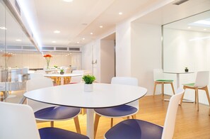 Una sala de conferencias moderna con una mesa redonda, sillas blancas y un panel de vidrio.
