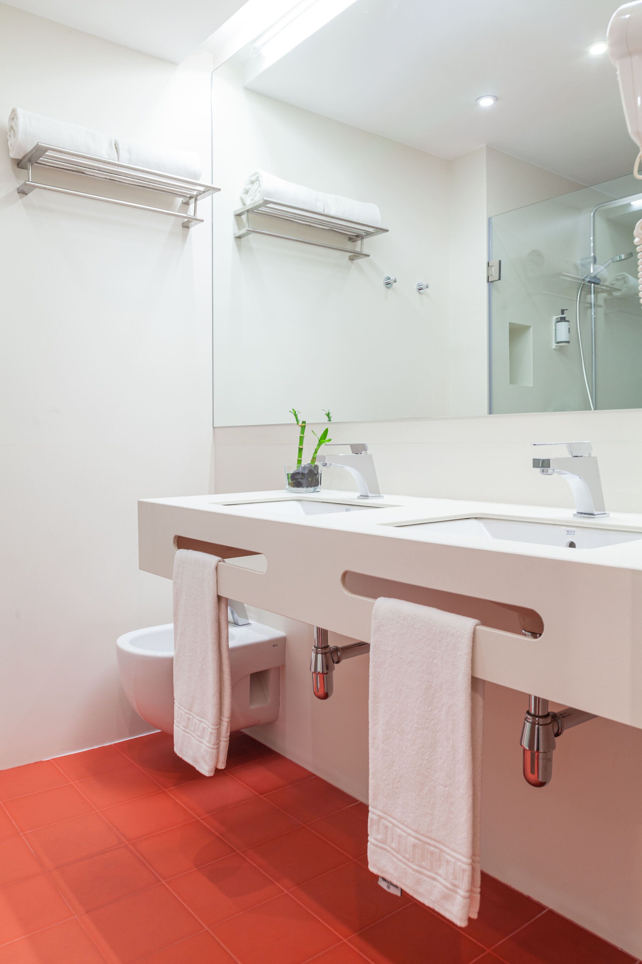 Een moderne badkamer met een witte wastafel, twee handdoekrekken, een toilet en een douchecabine met glazen wanden.