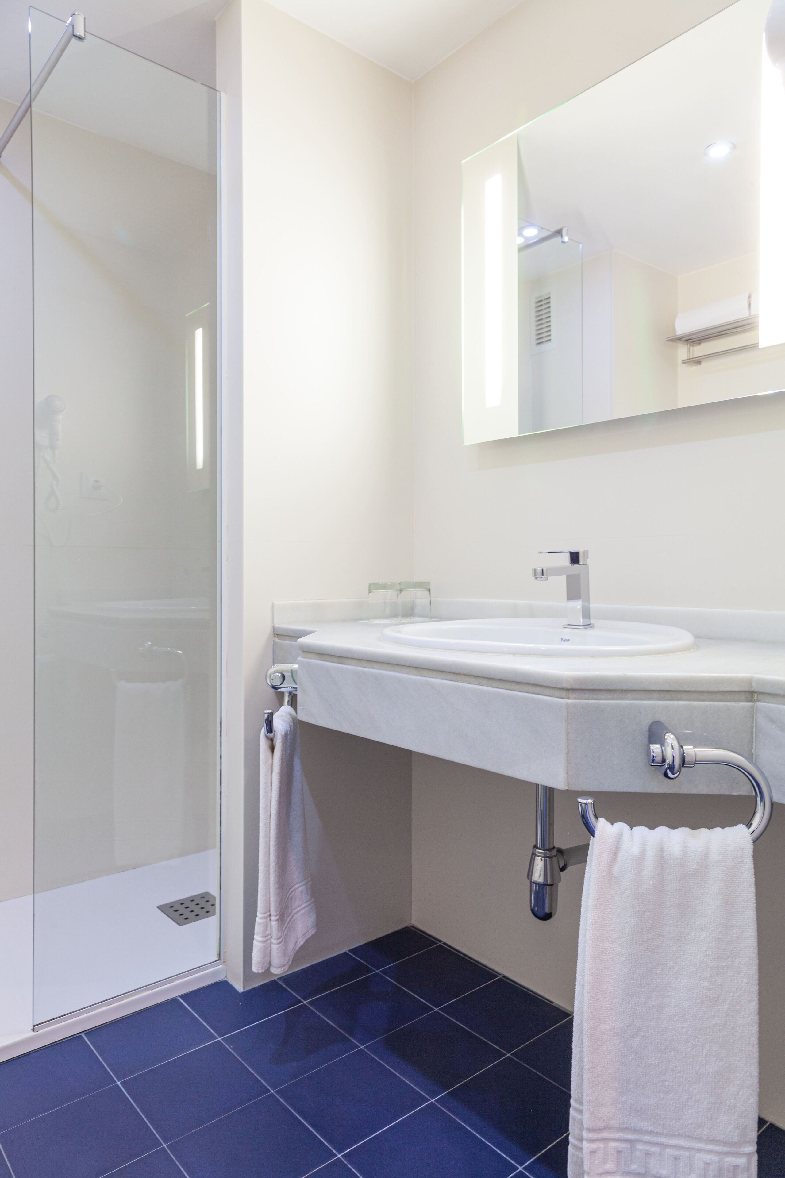 Un baño moderno con cabina de ducha de vidrio, un lavabo blanco y un espejo sobre él.