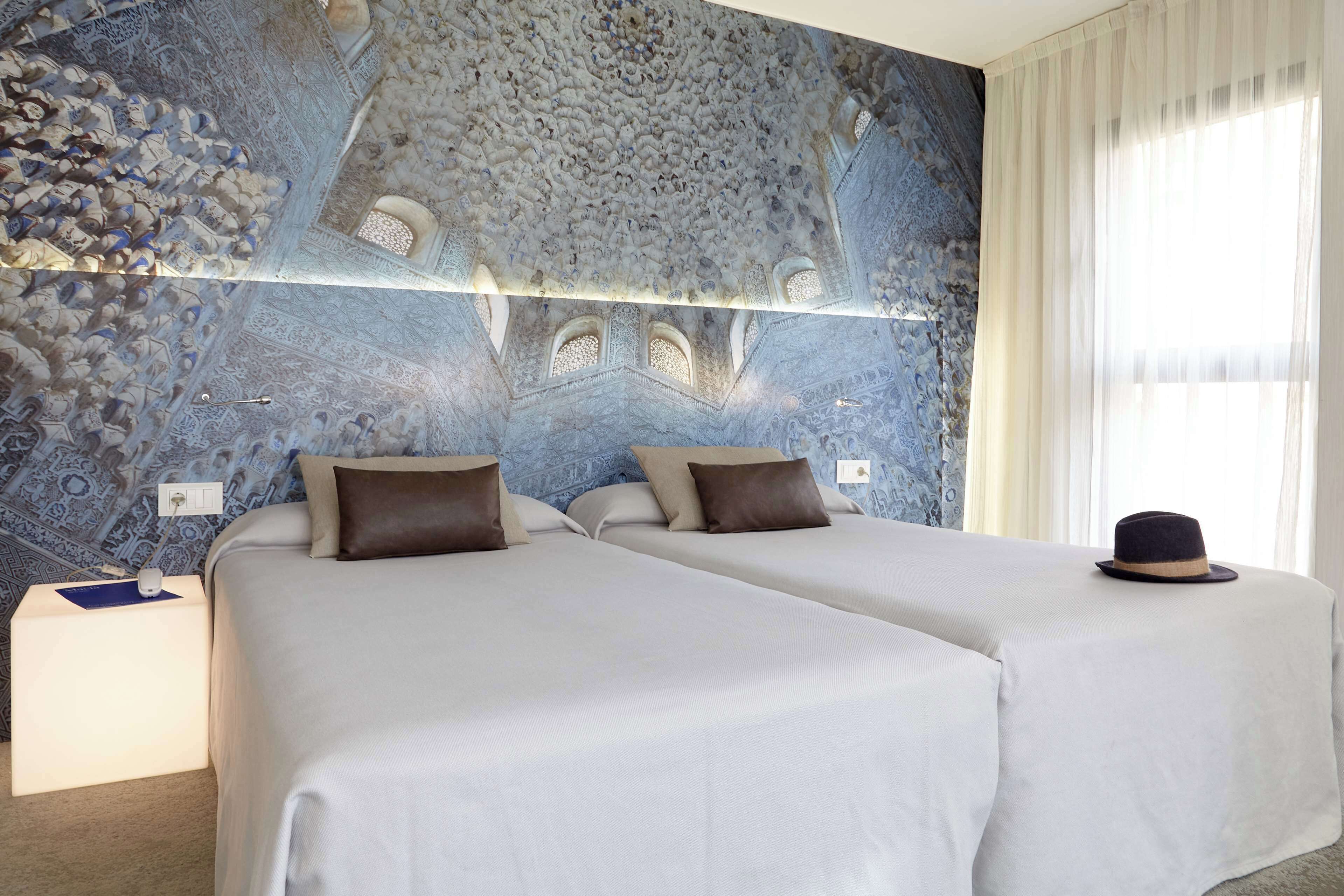 A hotel room with two beds, a decorative ceiling, and a window with curtains.
