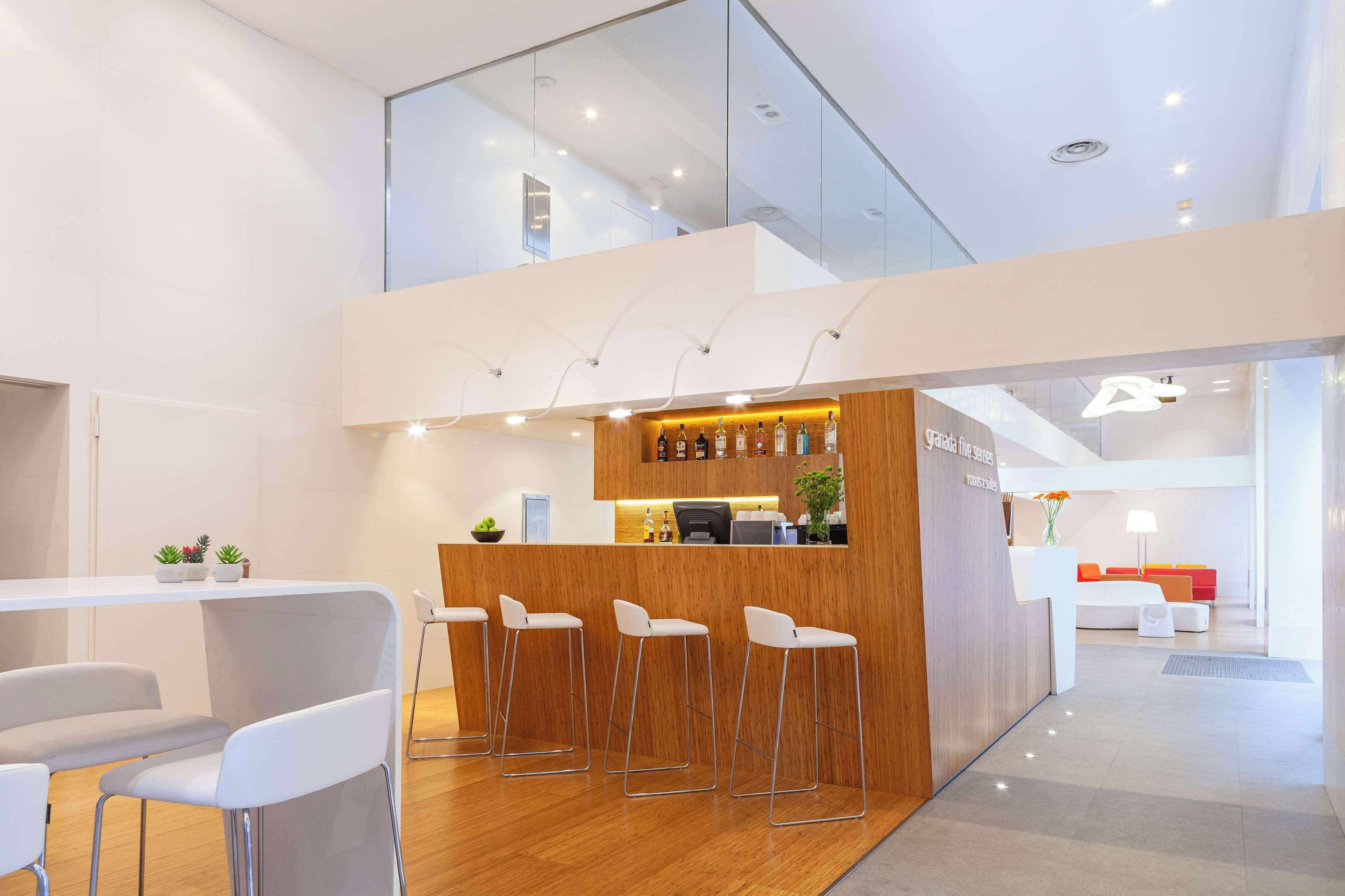 A modern reception area with a bar, white chairs, and a seating area with a red couch.