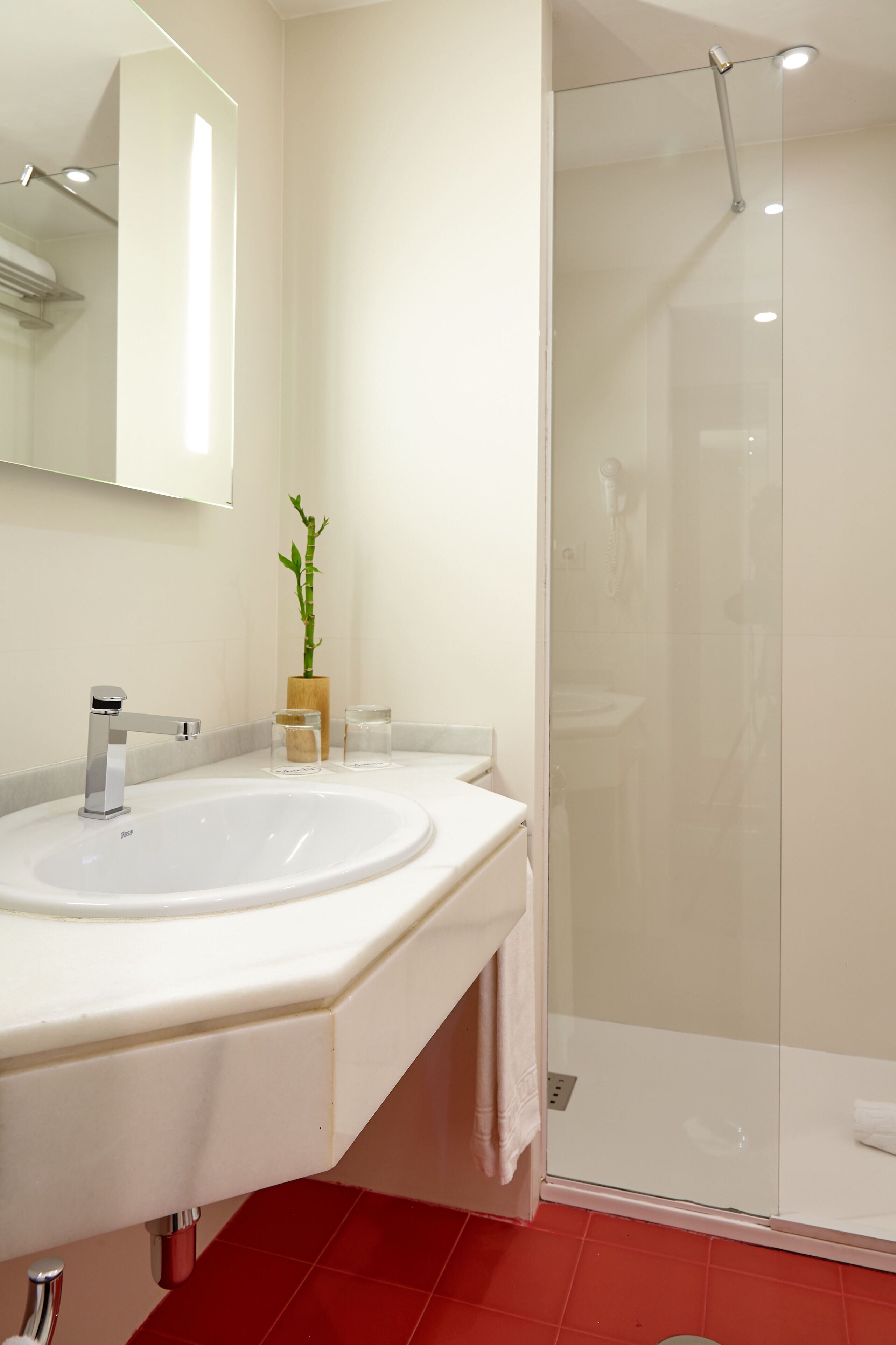 Un baño moderno con lavamanos blanco, cabina de ducha con mampara de vidrio y espejo sobre el lavamanos.
