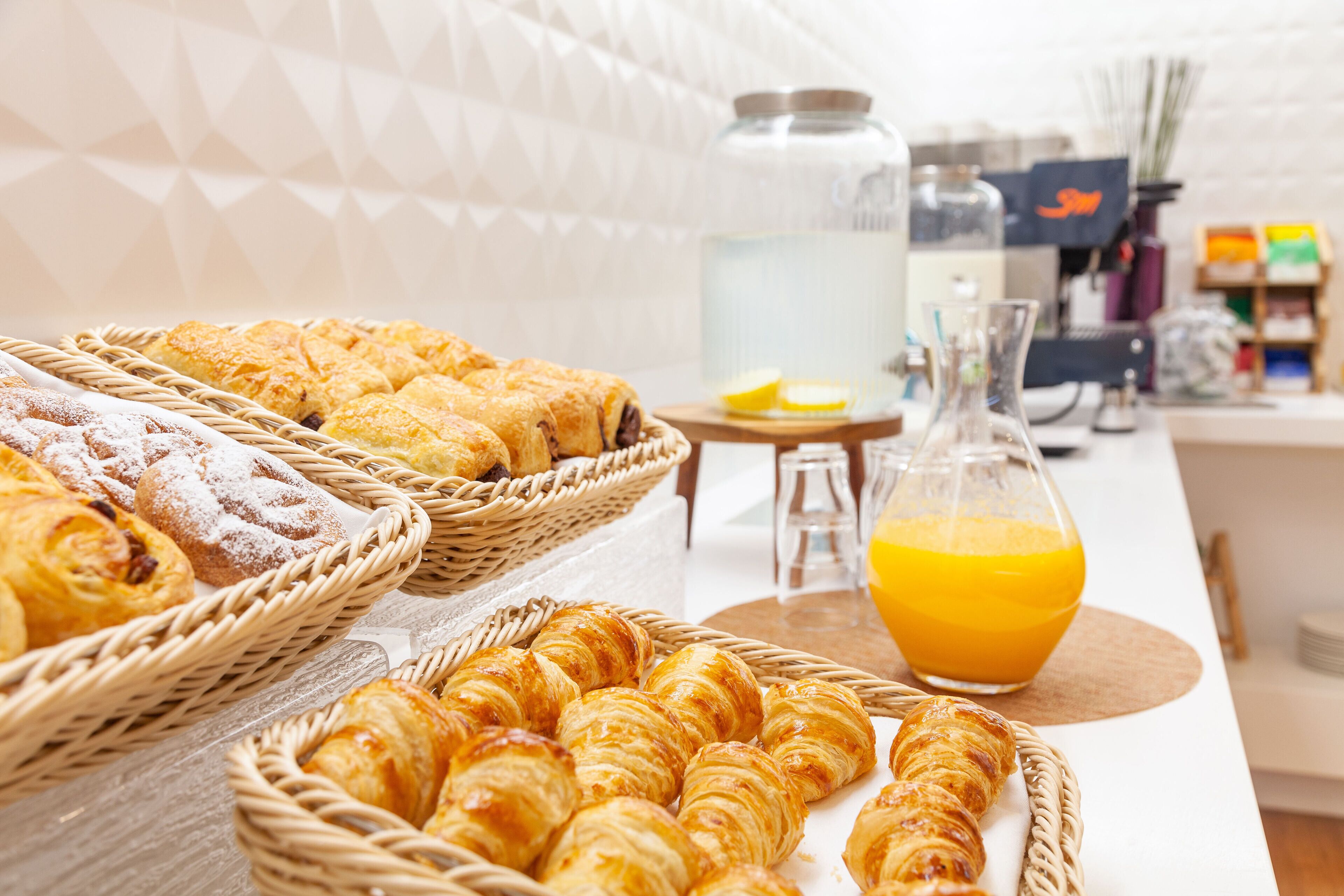 Un bufé de desayuno con fuentes de pastelería y una jarra de jugo de naranja.