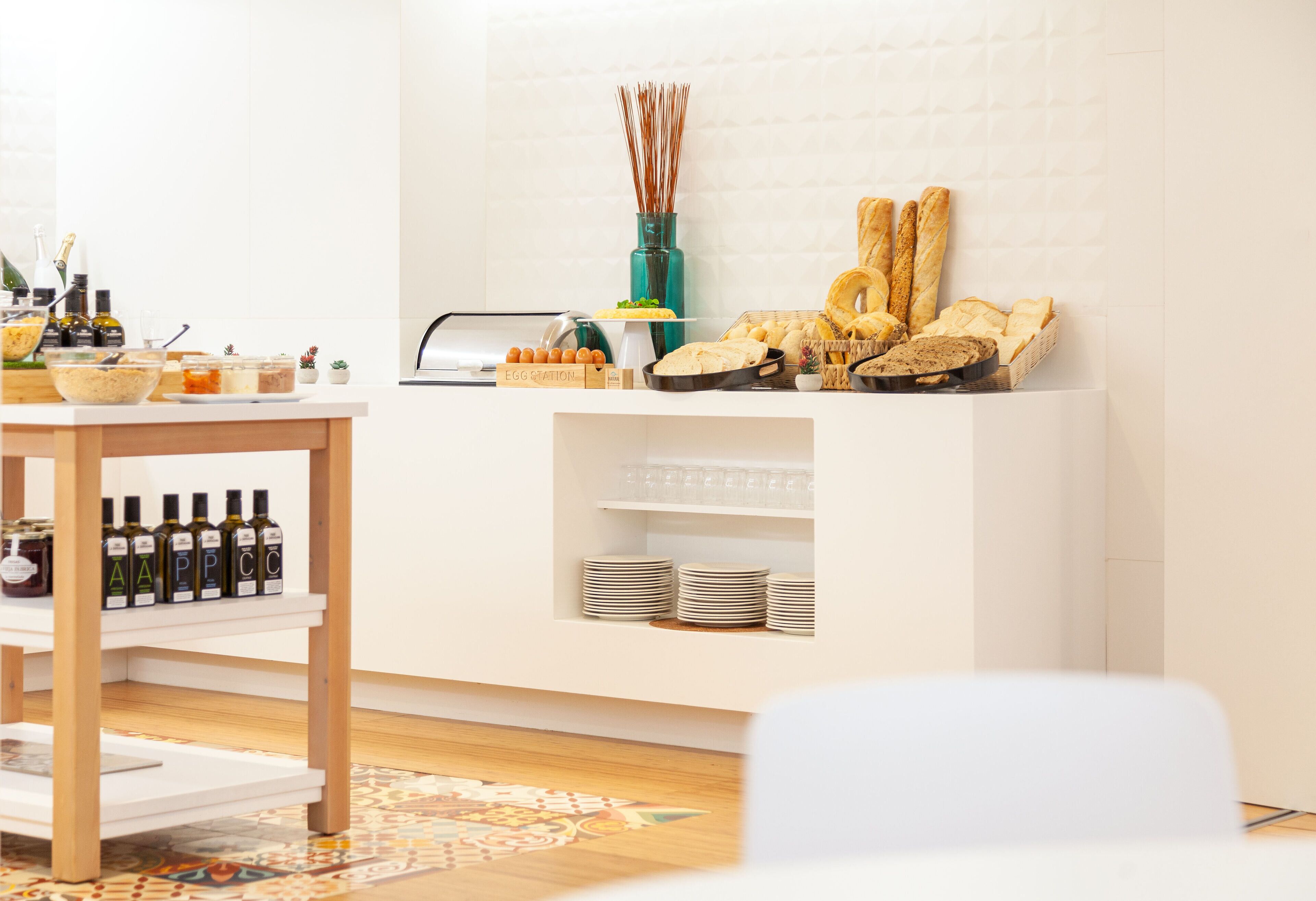 A modern kitchen with a white countertop, a wooden table, and a variety of food items and condiments.