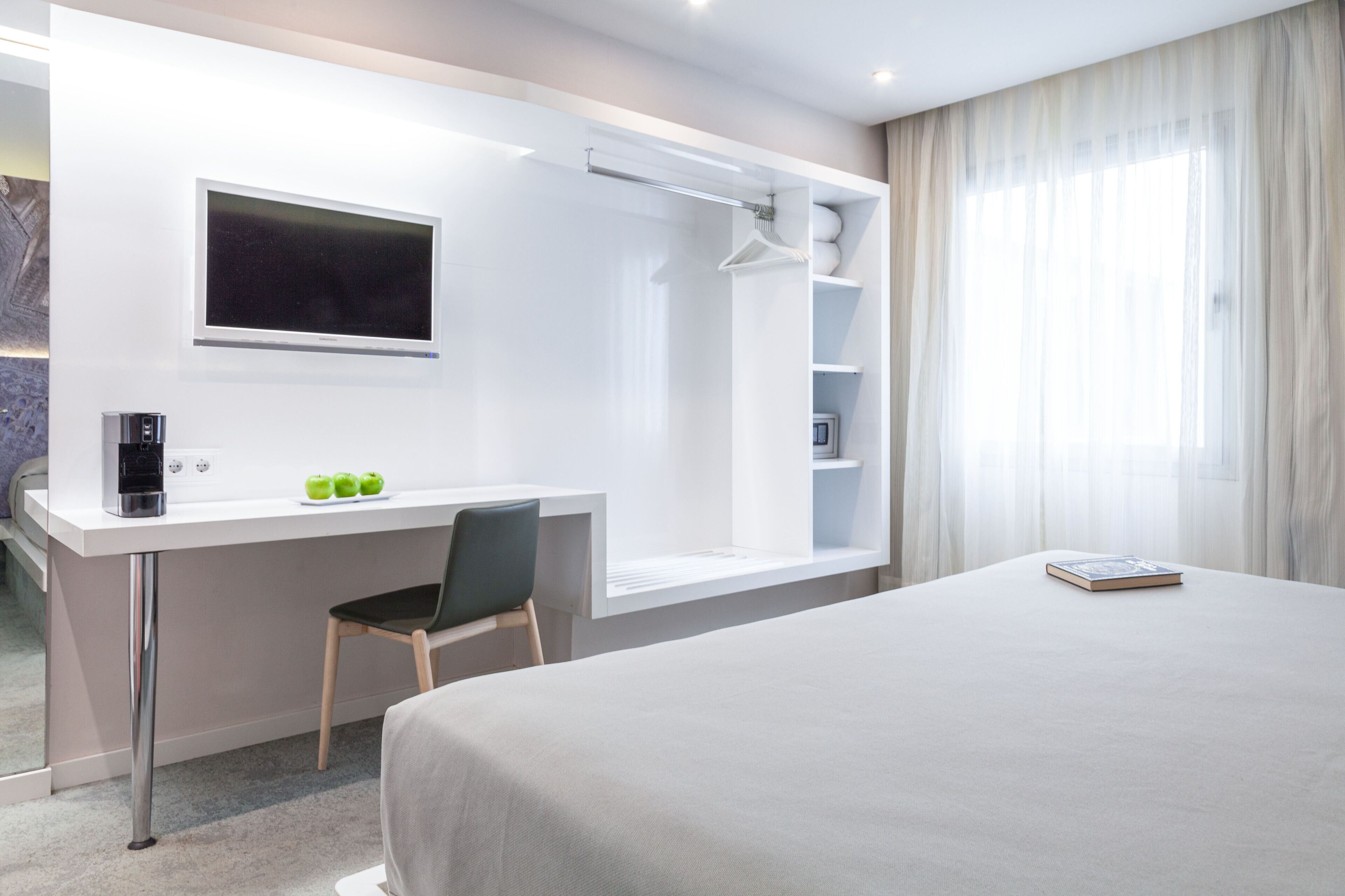 Una habitación de hotel moderna con una cama grande, un escritorio con cafetera, una silla, un televisor y zona de ducha.