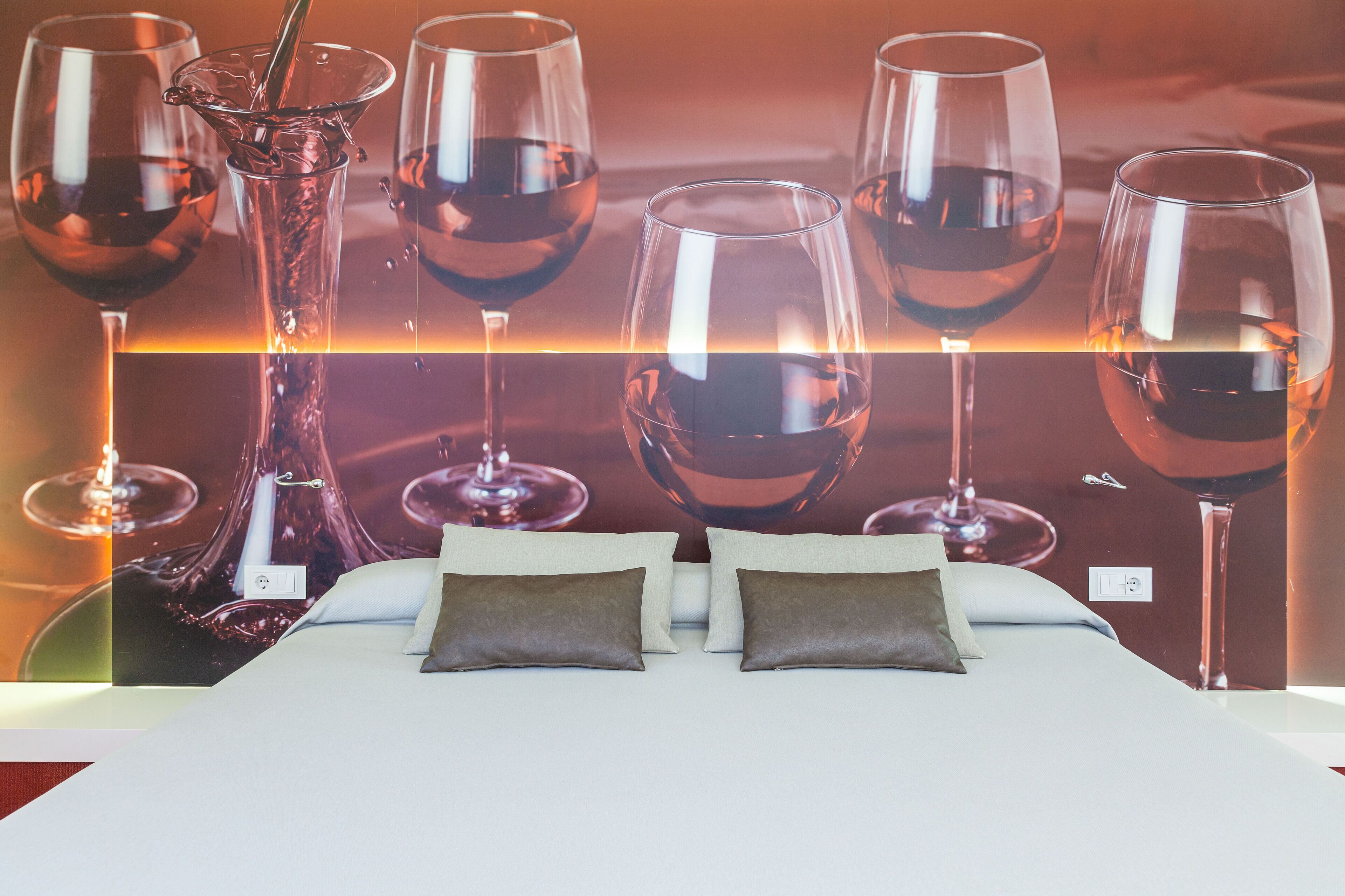 Un dormitorio con cama, almohadas y una pared con copas de vino.