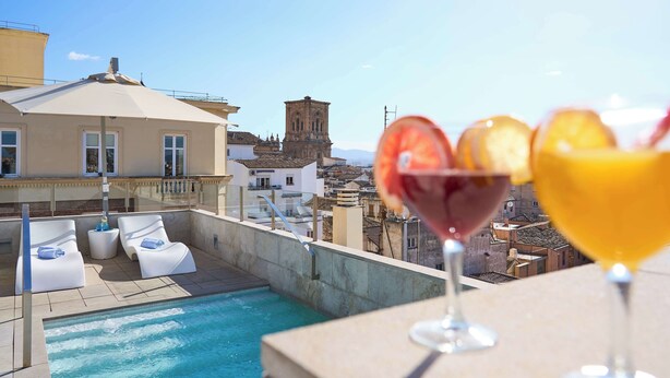 A rooftop pool area with lounge chairs, a pool, and a view of a historic tower. - Hotel Macià Granada Five Senses Rooms & Suites (Granada)