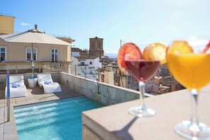 Zona de piscina en la azotea con sillones de descanso, piscina y vistas a una torre histórica.