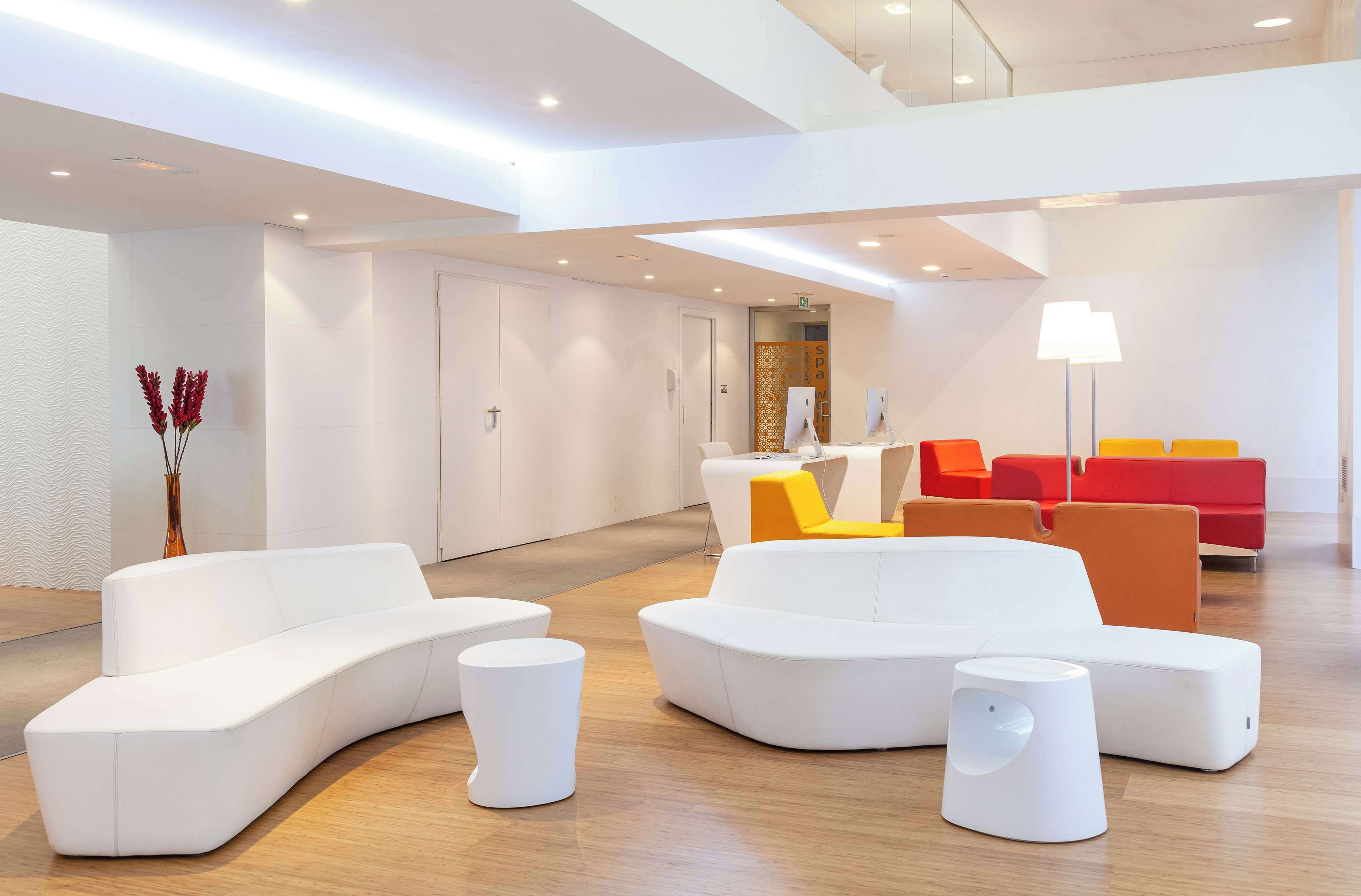 A modern lobby with white sofas, a yellow chair, and red seating.