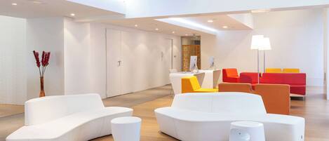 A modern lobby with white sofas, a yellow chair, and red seating.