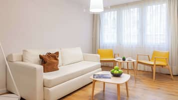 Una sala de estar moderna con un sofá blanco, sillas amarillas, una mesita con un cuenco de manzanas y una lámpara.
