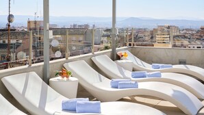 A rooftop lounge area with sun loungers, towels, and a drink. - Hotel Macià Granada Five Senses Rooms & Suites (Granada)