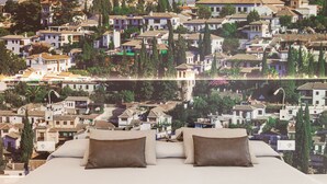 A bedroom with a bed, pillows, and a view of a town with buildings and trees. - Hotel Macià Granada Five Senses Rooms & Suites (Granada)