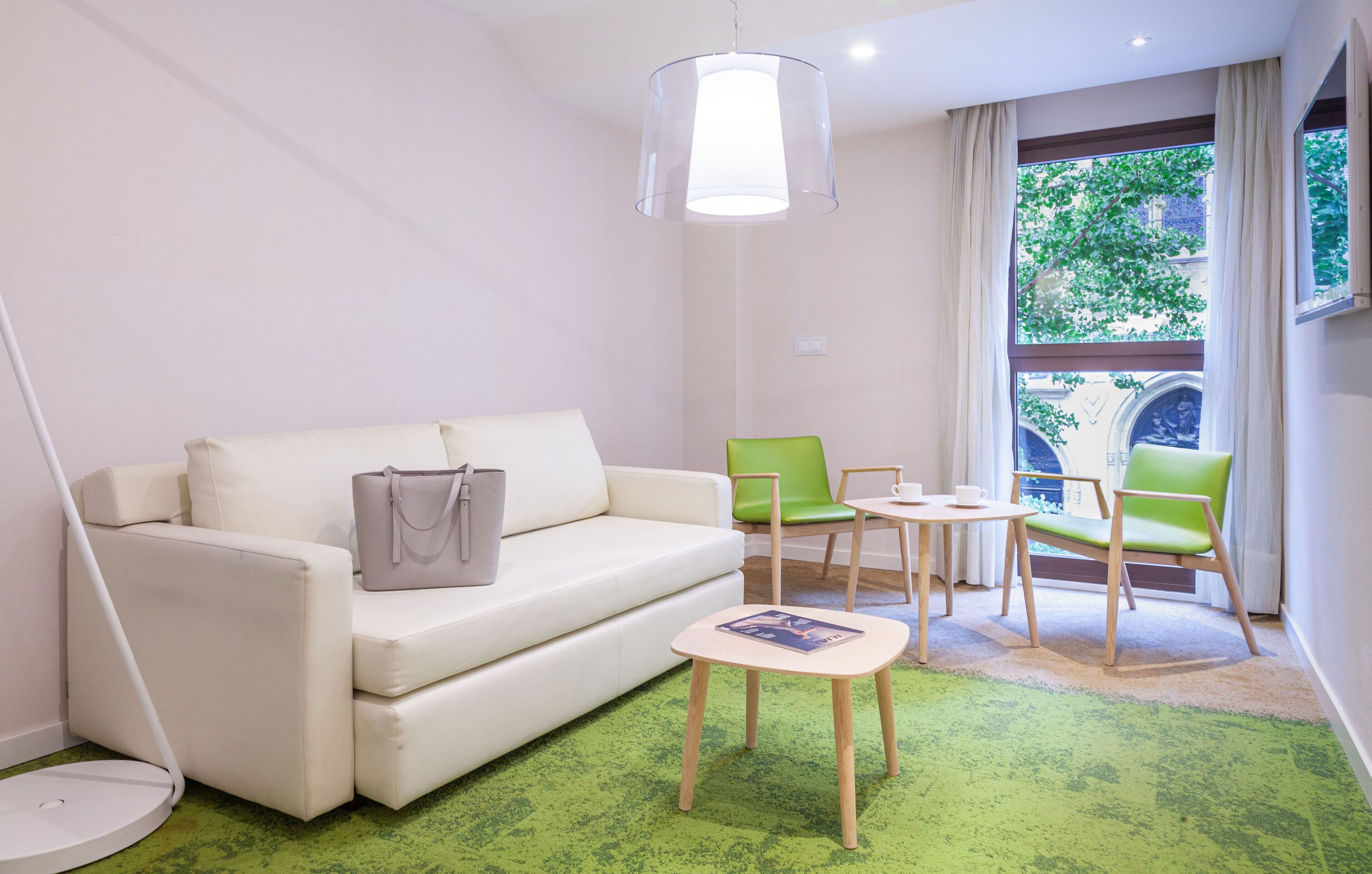 A modern hotel room with a white sofa, green chairs, a small table, and a green carpet.