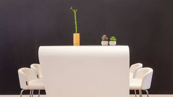 Una habitación moderna con una pizarra que presenta arte y texto hechos con tiza, una mesa blanca con dos plantas en macetas y sillas blancas con estructura metálica.