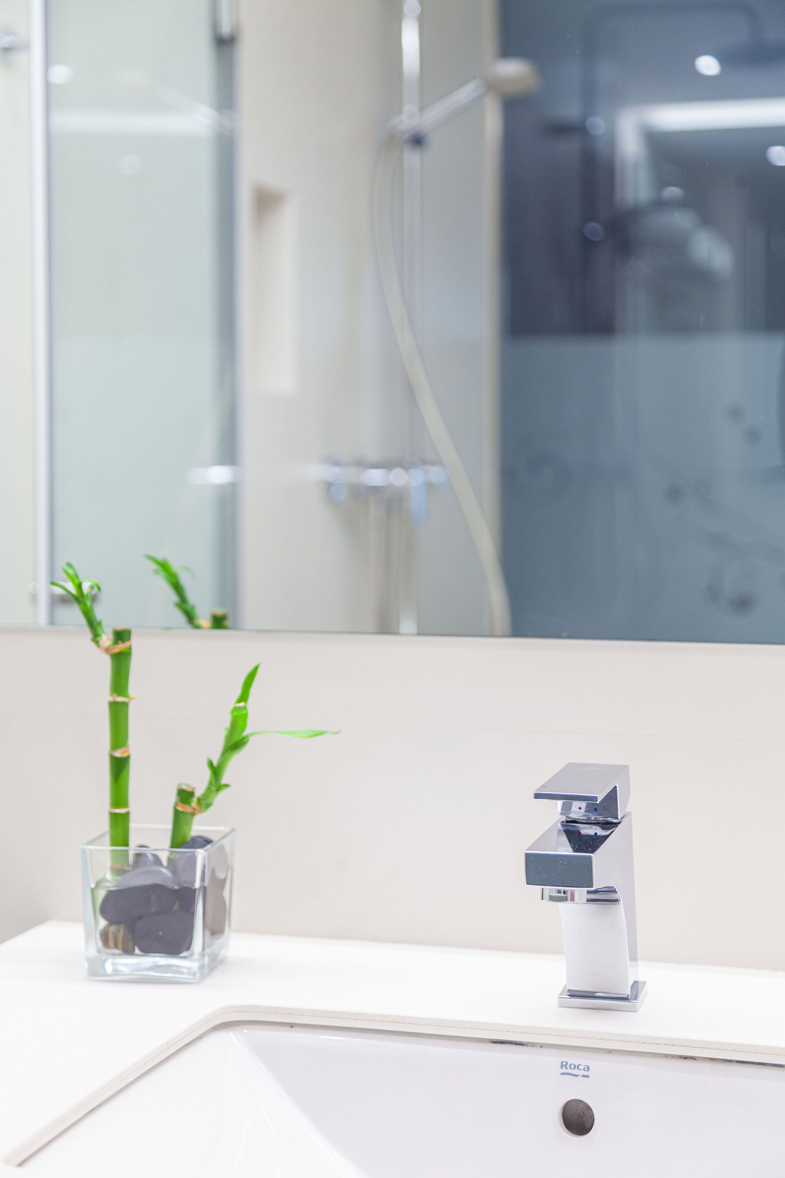 Ein Badezimmer mit einem weißen Waschbecken, einem Glasbehälter mit Pflanzen und einem modernen Wasserhahn.