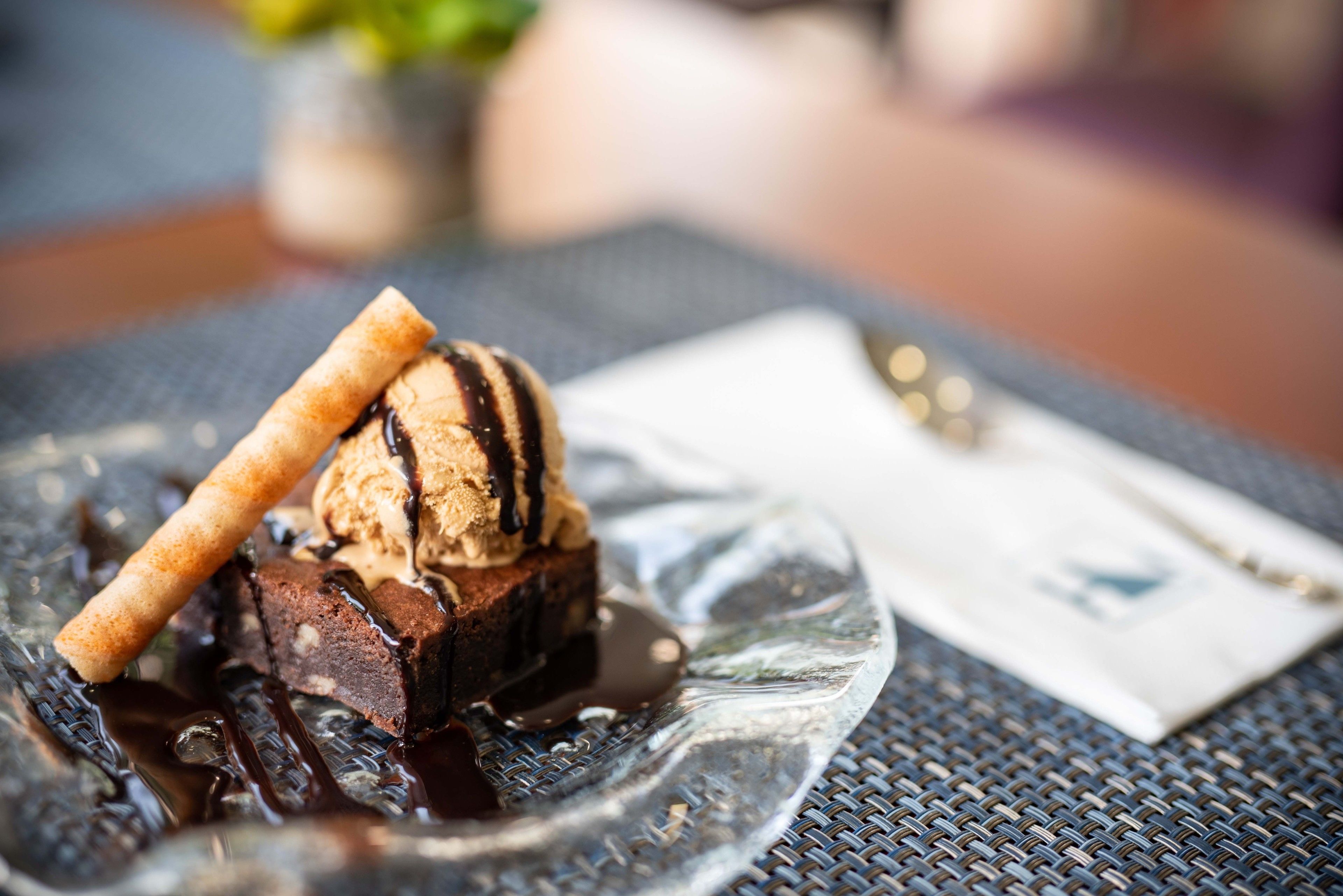 A dessert plate with chocolate cake, ice cream, and a wafer stick on a textured table.
