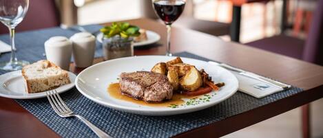 Una mesa de comedor con un plato de comida, una copa de vino tinto y un tenedor.