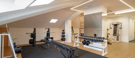 A modern gym with a sloped ceiling, weightlifting equipment, and a mirror wall.