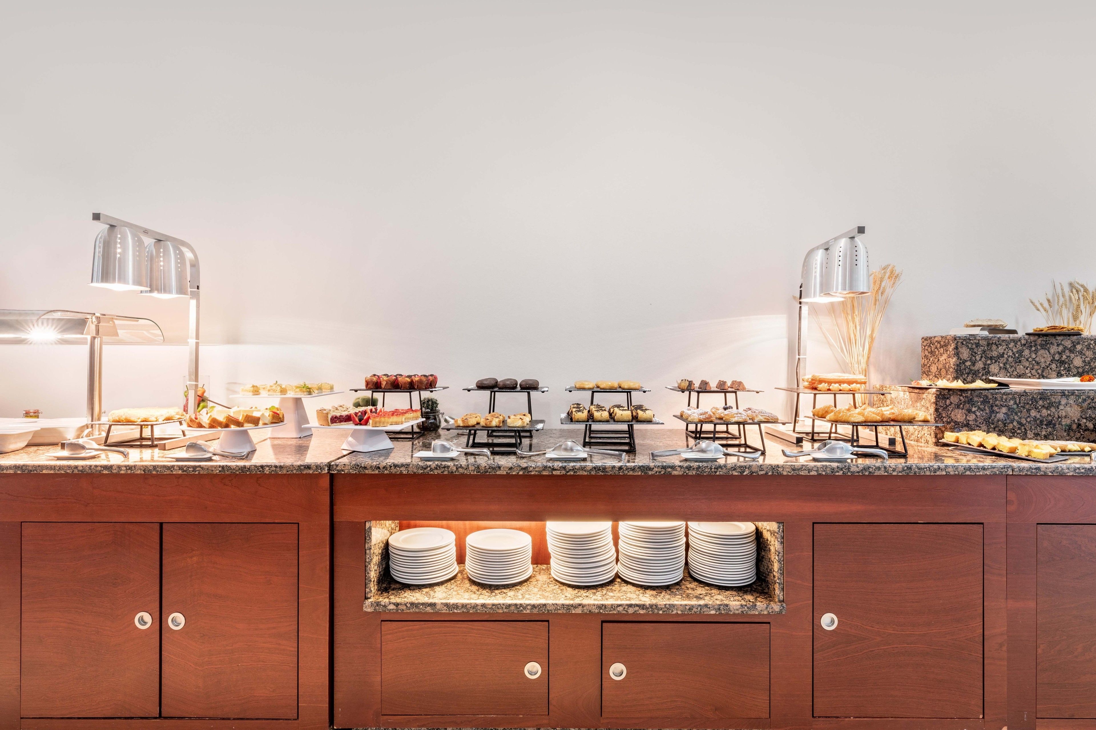 A buffet setup with various food items and a stack of plates in a wooden cabinet.