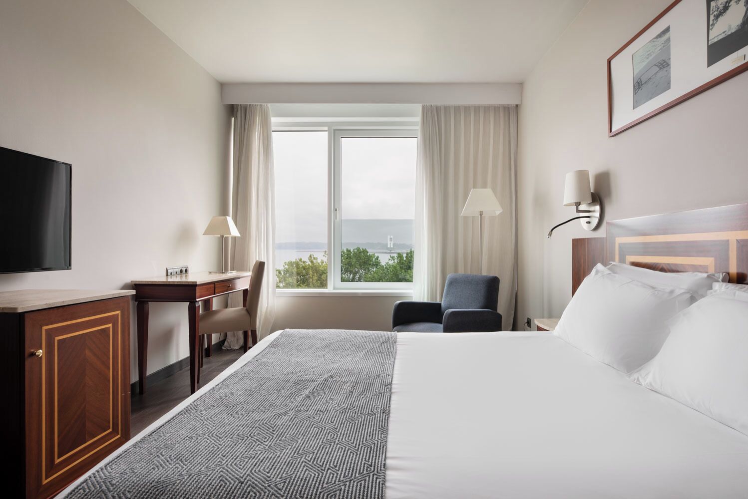 A hotel room with a bed, desk, chair, TV, and a window with a view.