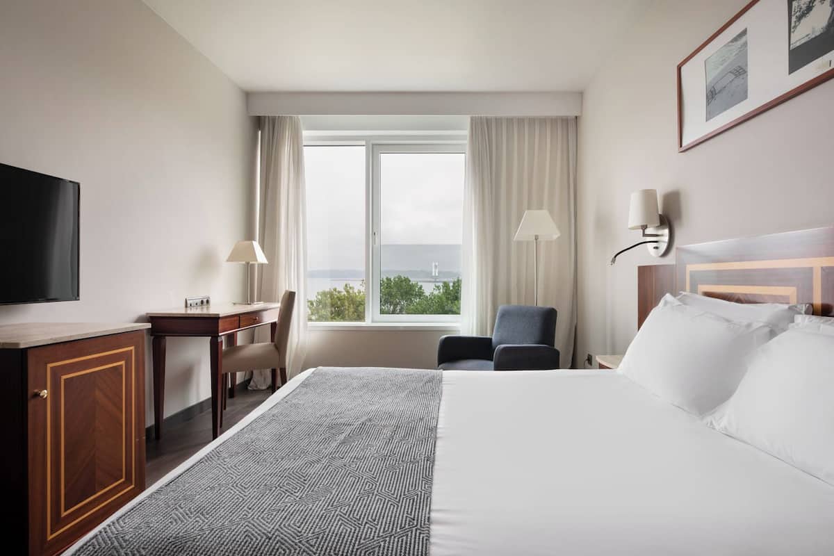A hotel room with a bed, desk, chair, TV, and a window with a view.