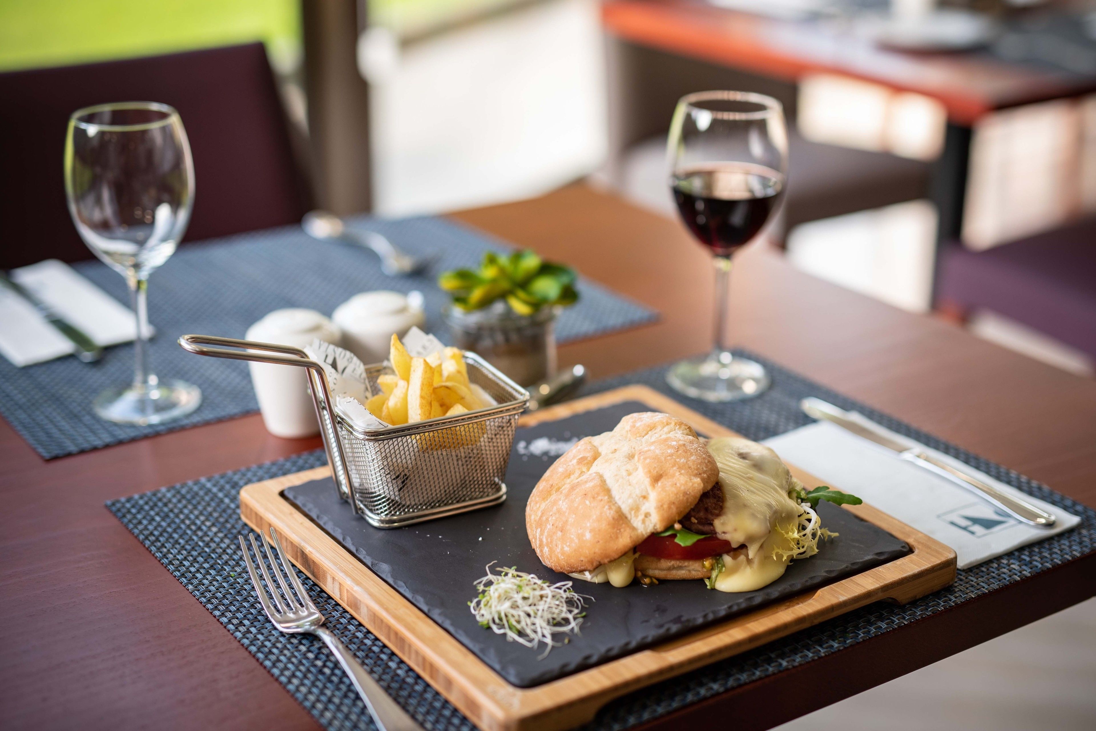 A dining table with a burger, fries, and wine glasses.