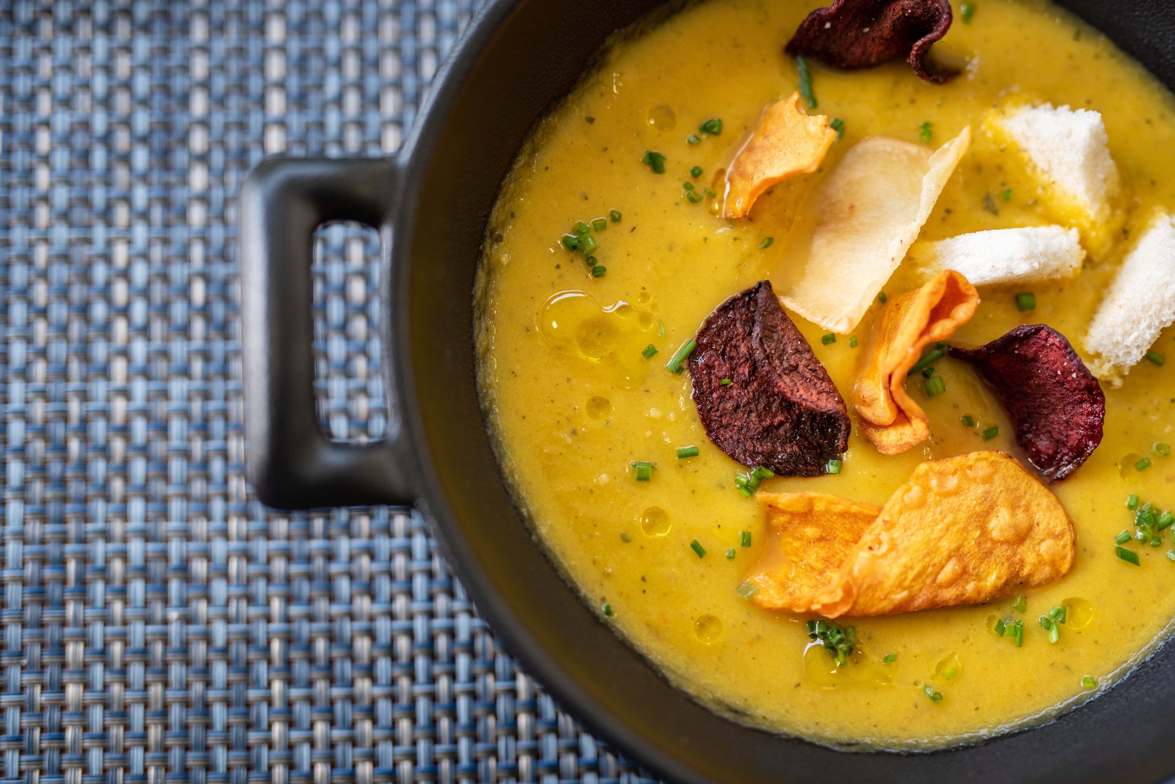 Un bol de soupe, accompagné de pain et de saucisses, est posé sur un tapis tressé.