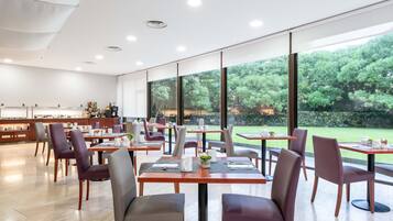 Un comedor moderno con mesas y sillas, ventanas amplias y vistas a zonas verdes exteriores.
