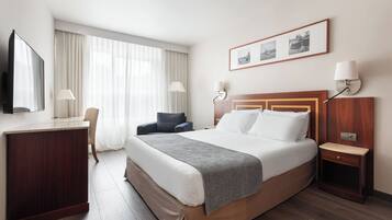 A hotel room with a large bed, a desk, a chair, a TV, and a window with curtains.