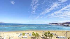 Una playa con cielo despejado, aguas tranquilas y una orilla arenosa con sombrillas y sillas de descanso.