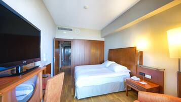Habitación de hotel con cama, escritorio, silla, televisor y lámpara.