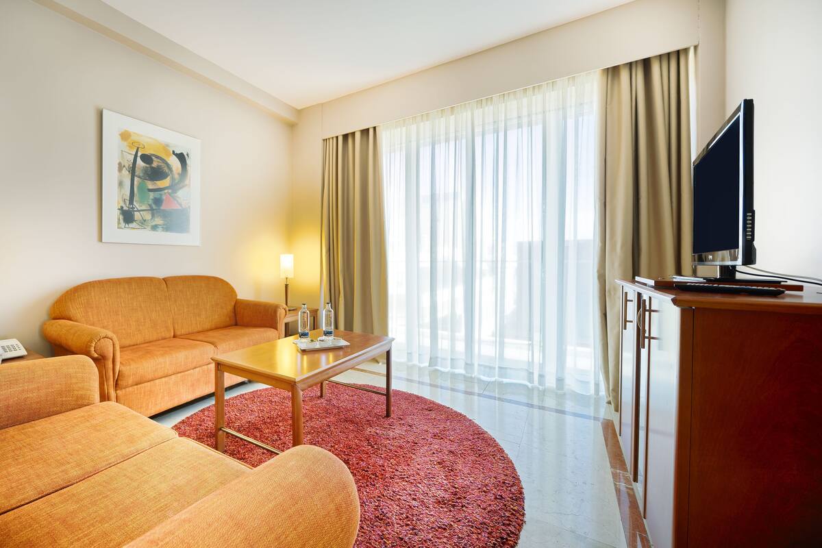 Une chambre d’hôtel avec un canapé, une table basse, une télévision et un tableau au mur.