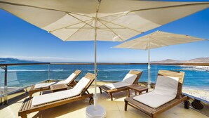 Una terraza con sillones de madera y sombrillas grandes, con vista a la playa y al océano.