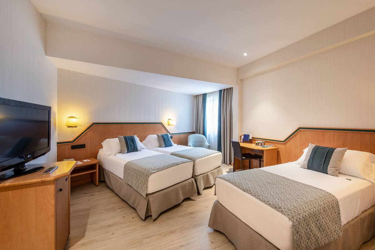 A hotel room with two beds, a TV, a desk, and a chair.