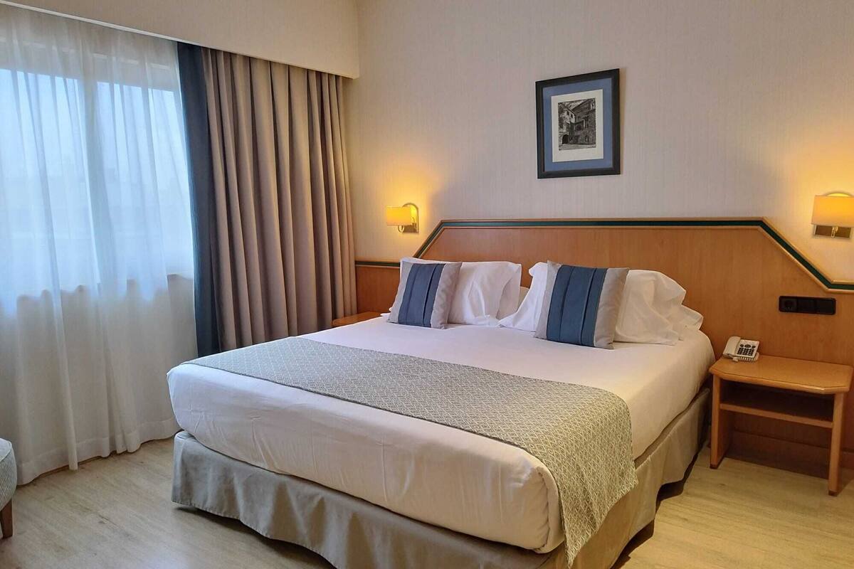 A hotel room with a large bed, a bedside table with a lamp, a phone, and a picture on the wall.