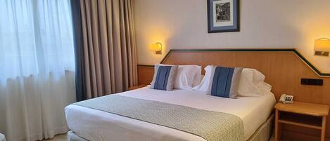 Habitación de hotel con una cama grande, una mesita de noche con lámpara, un teléfono y un cuadro en la pared.