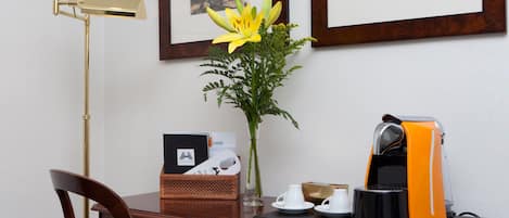 A wooden desk with a vase of yellow flowers, a coffee maker, and a framed picture on the wall.