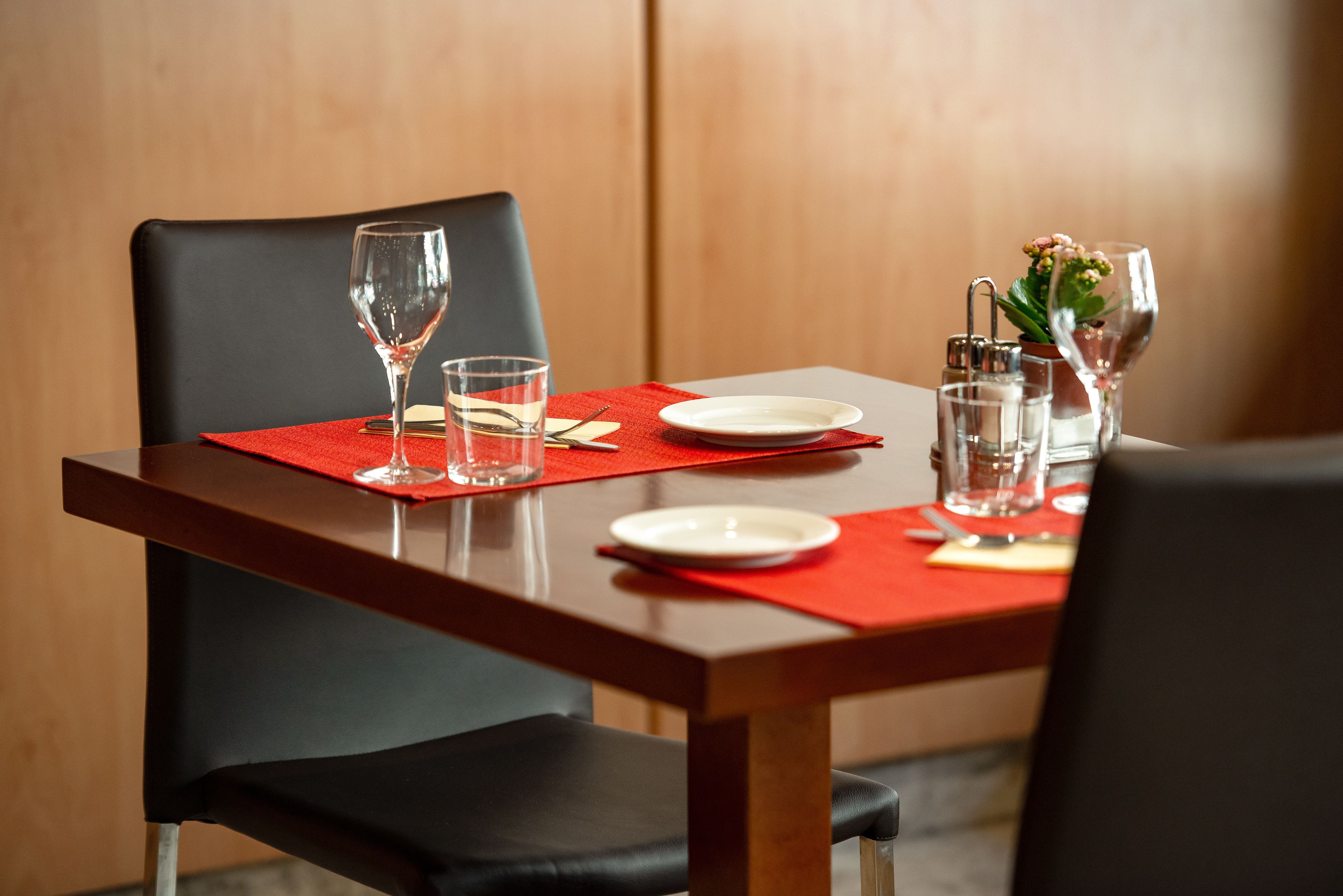 A dining table set with a red placemat, clear glasses, a white plate, and a small potted plant.